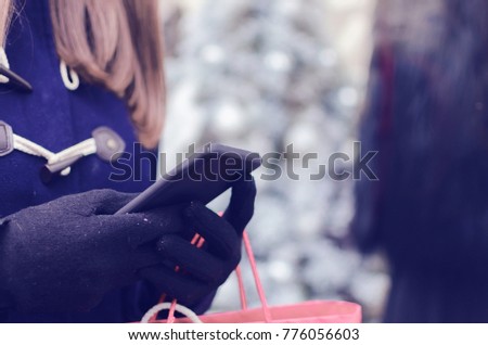 Hands of a shopper buying on line holding shopping bags and mobile phone on the street in winter time.
