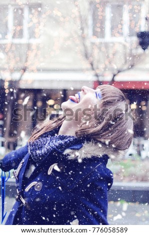 Amazing young woman having fun on snowy day. Girl eating snowflakes with tounge outside. Christmas time
