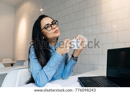 young business woman in glasses and blue shirt working on laptop in cafe and drinking delicious coffee
