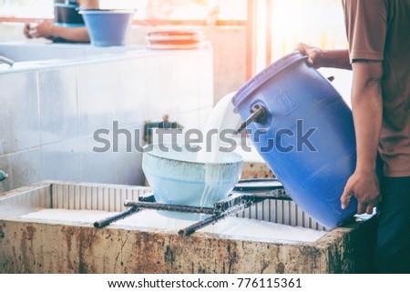 Rubber production. Pouring the natural rubber latex into container through filter  in the small rubber factory. Royalty-Free Stock Photo #776115361