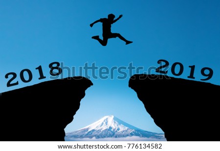 A young man jump between 2018 and 2019 years over the sun and through on the gap of hill silhouette evening colorful moutain. happy new year 2019. Royalty-Free Stock Photo #776134582