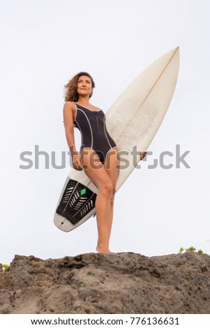 Surf girl with long hair go to surfing. Sporty surfer woman holding blank white short surfboard on a rock at sunset or sunrise. Bali island, Indonesia. Outdoor Active Lifestyle. It's time for surfing!