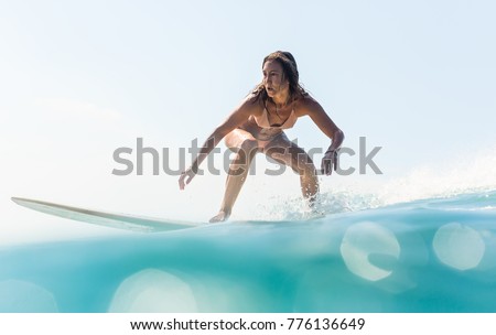 Beautiful young brunette girl in a bikini swimsuit ride big wave. Sporty surfer woman surfing in Mauritius in the Indian Ocean on the background of blue sky, clouds and transparent waves. Hippie life.