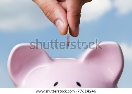 Saving, male hand putting a coin into piggy bank.