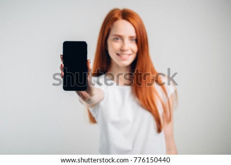 Happy woman showing blank smartphone screen over white background. Focus on smartphone.
