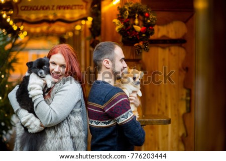 Christmas holidays. Young couple on the Christmas bazaar with pets. Two little spitz-dogs on hands at the owners.