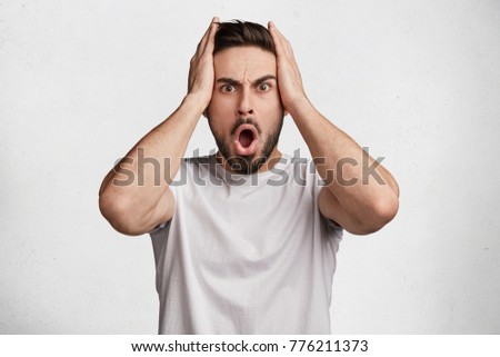 Image of terrifed shocked man has some problems, keeps hands on head, being shocked hearing awful news about relatives or friends. Depressed surprised male has negative reaction on something Royalty-Free Stock Photo #776211373