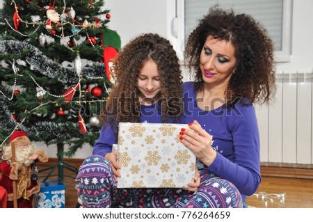 Smiling girl taking gift from her mom. Mom giving present to a happy child