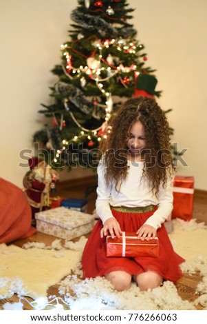 Portrait of little girl wait a New Year With Under a Christmas tree. Cute girl holding Christmas gift