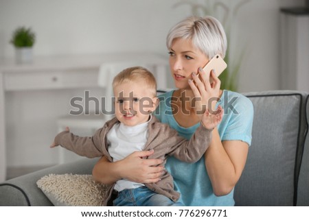 Young mother talking on phone while holding her baby at home