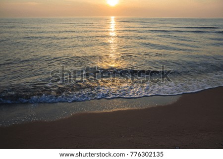 Morning sunrise light shining on ocean wave and sand.