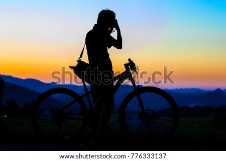 Silhouette of photographer in action take photo with bike on mountain with sunrise.