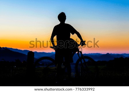 Silhouette young man and bike on muontain, sunset.