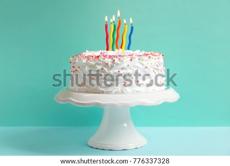 Stand with birthday cake and candles on table against color wall