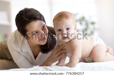 Mom and her little son weared diaper on bed. Mother embracing infant baby boy.