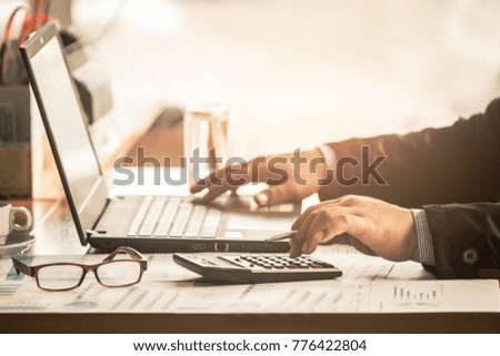 A businessman calculating about cost with using laptop searching data and touch calculator in office.