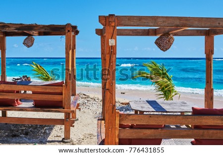 Romantic gazebo lounge at tropical resort. Empty wooden lounge beds on a beautiful beach on the background of a shining turquoise ocean. Summer morning. Relaxing private sunbed on beautiful beach. 