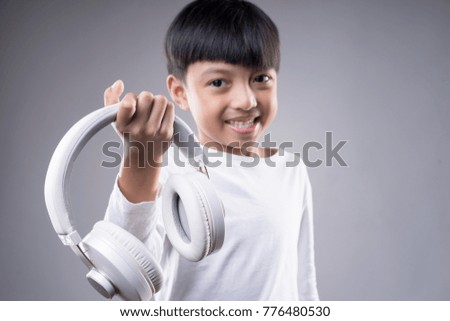 Asian boy wearing a wireless headphone and enjoying music on a grey background.
