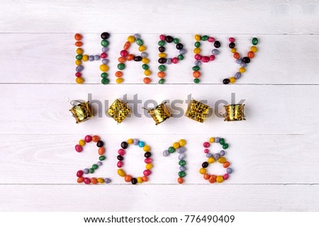 The inscription "Happy 2018" from sweet colored jelly beans. Small toy gifts in gold wrapping paper. A typical New Year's, Christmas still-life. Small toy golden drums for a Christmas tree.
