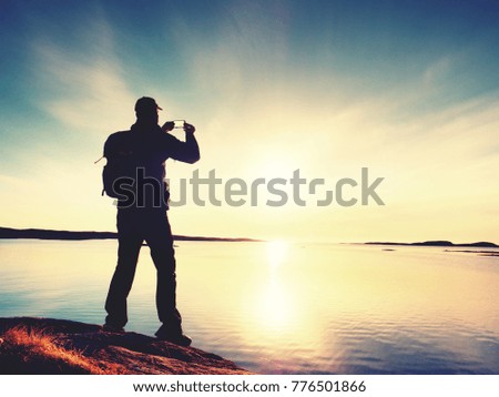 Silhouette of man keep memories with camera phone in his hand. Marvelous sunset at sea, smooth water level