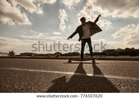Every morning routine of professional rider practicing skills using longboard outdoors. Summer lifestyle picture of stylish European guy performing stand slide on skateboard along empty country road  