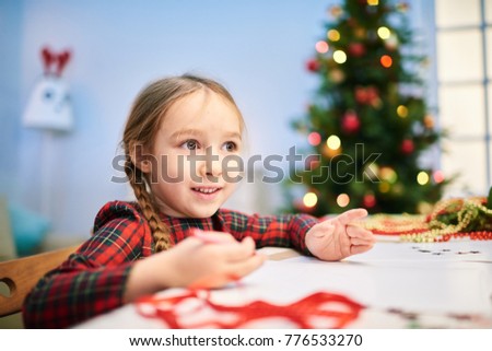 Creative little girl drawing Christmas card for her granny with wax crayons while sitting at desk of cozy living room, portrait shot