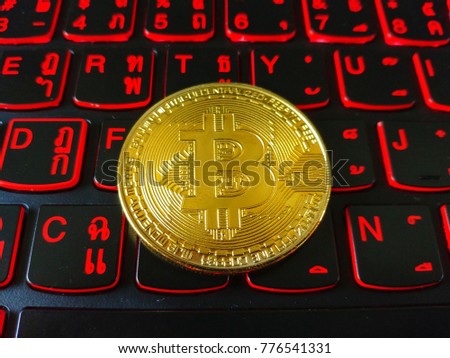 Golden bitcoin on red backlit black Thai keyboard. Bitcoin is a cryptocurrency and worldwide payment system. It is the first decentralized digital currency, as the system works without a central bank.