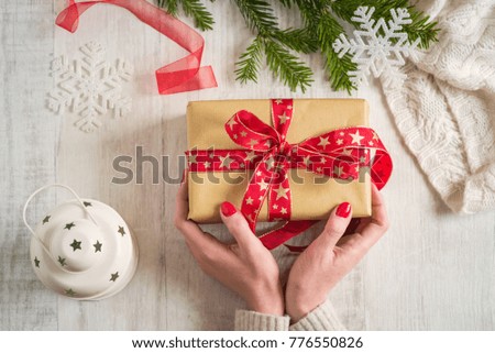 Woman holding a Christmas gift in hand on wooden background