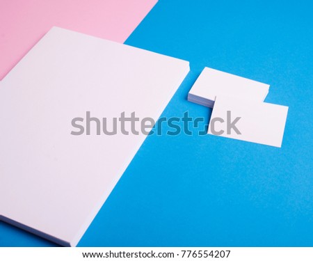 Business cards and stacked sheets of paper in white on pink and blue background. Mockup.