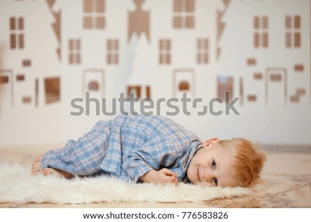 Cute blonde hair little boy in sleepwear near christmas toy paper houses