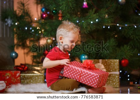Cute blonde hair little boy near the fireplace and gifts under Christmas tree