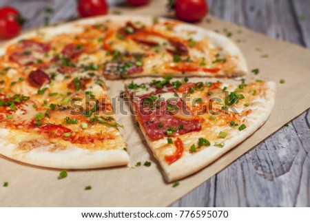 Pizza with a thin crust with cheese, bacon, pepper and herbs on a light, wooden background