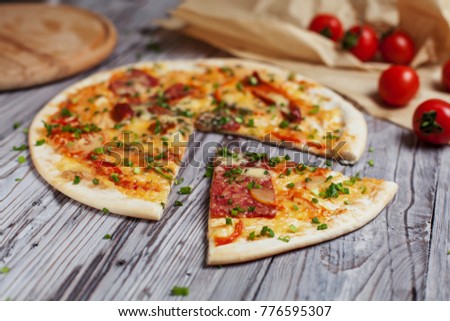 Pizza with a thin crust with cheese, bacon, pepper and herbs on a light, wooden background