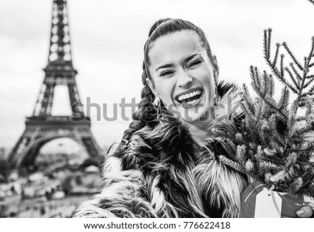 The Party Season in Paris. Portrait of smiling trendy fashion-monger with Christmas tree in fur coat in Paris, France taking selfie