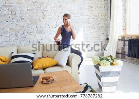 Female freelancer in her casual home clothing working remotly from her dining table in the morning. Houses on a sofa on a white brick wall background. Architect, blueprints. talking on the phone