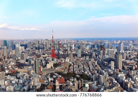 Beautiful city skyline of Downtown Tokyo under blue sunny sky, with landmark Tokyo Tower standing tall among crowded high-rise buildings and Odaiba seaside area lying in Tokyo Bay in distant horizon