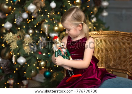 The girl is sitting by the decorated Christmas tree with a wooden soldier. Christmas and New Year