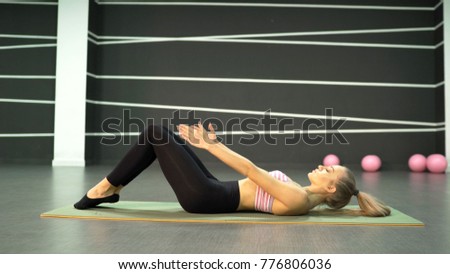 
the girl is engaged in pilates. The coach shows the Pilates exercise. The girl in the gym is on the floor. Girl doing stretching.