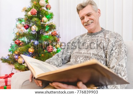 The old man look to a photo album near the christmas tree