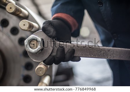 Mechanic repairman at the factory screws big bolt with large and heavy wrench key, holding it with both hands Royalty-Free Stock Photo #776849968