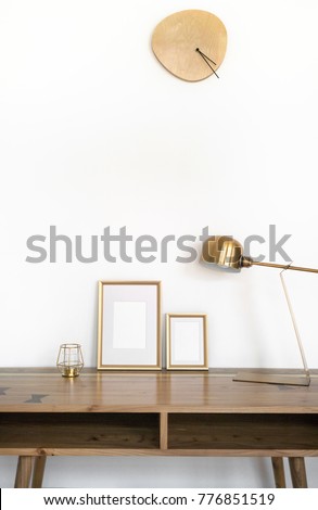 Modern home decor mock-up. Golden frames on wooden design table with gold metal lamp, candle and wooden clock on the wall. White background styled minimal interior mockup.