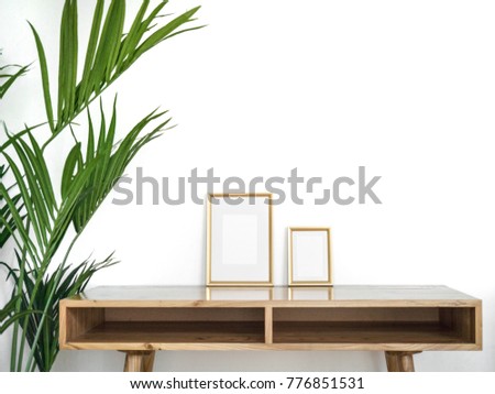 Modern home decor mock-up. Golden frames on wooden design table with green tropical plant near. White background styled minimal interior mockup.