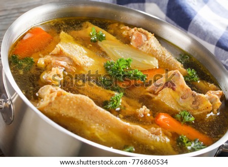 delicious Chicken soup with pieces of chicken meat on bone and vegetables in a metal casserole, view from above, close-up