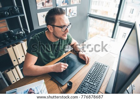 Top view of orderly bearded male working with screen of computer while locating at table in office. Profession concept