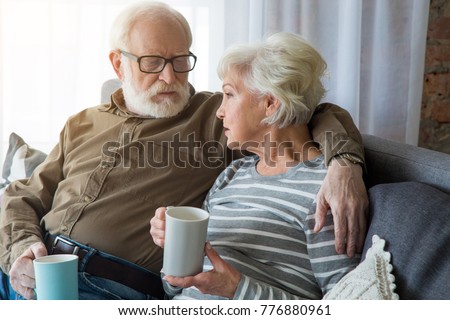 Honest conversation. Portrait of senior couple having dialogue at home while sitting on couch. Husband is cuddling wife while they holding hot cup of tea Royalty-Free Stock Photo #776880961