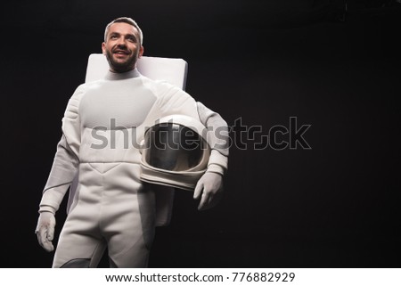 Portrait of cheerful spaceman is standing in hyperbaric astronaut protective suit and looking ahead with bright smile. He is holding white helmet. Isolated background with copy space in right side