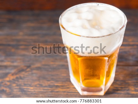 Top view of big glass with a light beer and a large head of foam on old dark desk. Drink and beverages concept