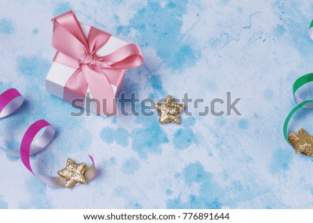 Bright colorful carnival or party scene of gift box, streamers and confetti on blue table. Flat lay style, birthday or party greeting card with copy space.