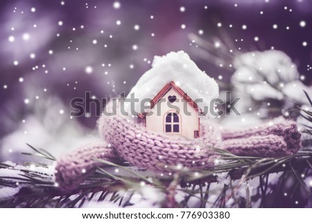 Christmas Toy house is wrapped in a warm scarf, it's snowing.on a natural natural background of a real fir in the snow, toned. Concept of winter, Christmas, new year,
 warm, cozy, loving, protecting  Royalty-Free Stock Photo #776903380