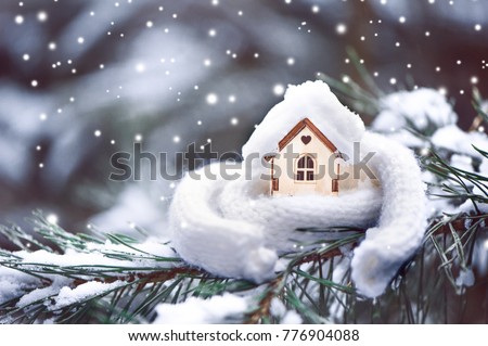 Christmas Toy house is wrapped in a warm scarf, it's snowing.on a natural natural background of a real fir in the snow, toned. Concept of winter, Christmas, new year,
 warm, cozy, loving, protecting t Royalty-Free Stock Photo #776904088